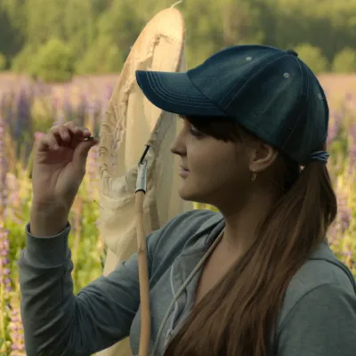 Profile of a student with long hair looking at a bug. An insect net is on her shoulder.